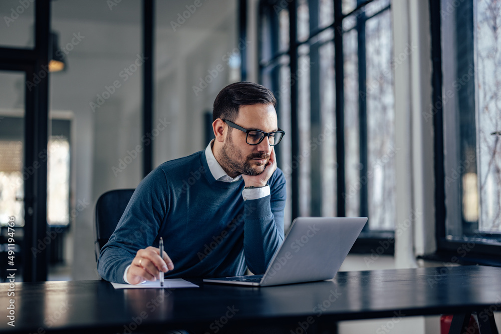 Serious caucasian insurance salesman, checking his client status, on his laptop.