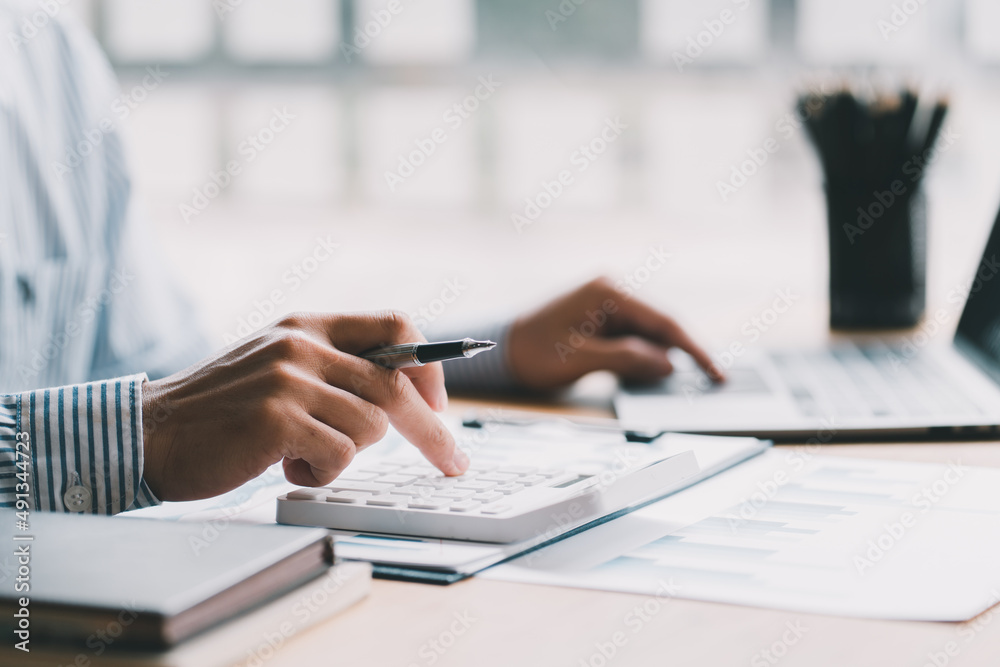 Close up of businessman or accountant hand holding pencil working on calculator to calculate financi