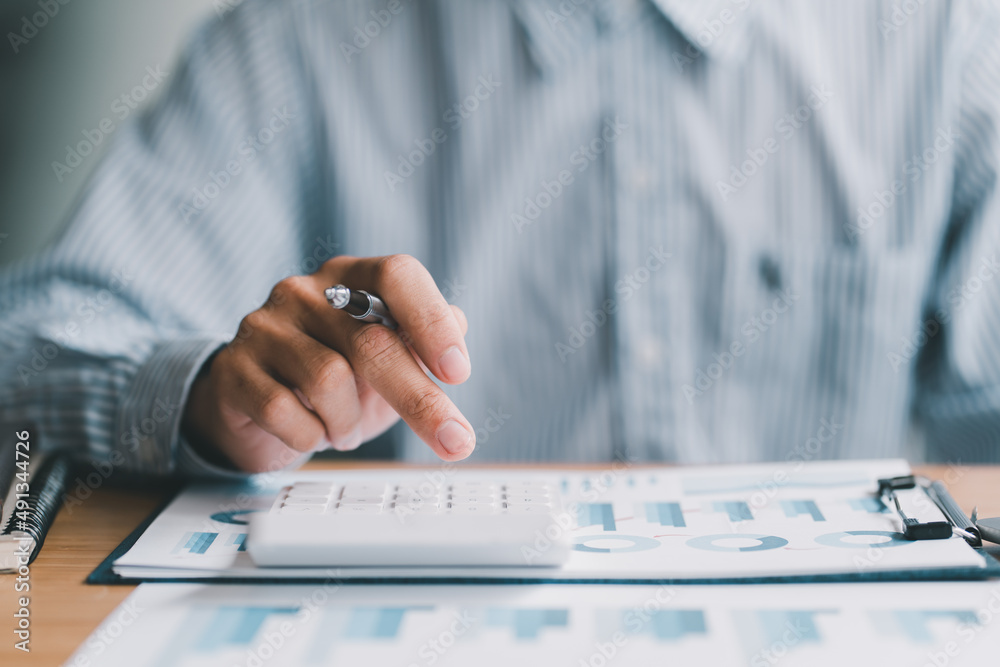 Close up of businessman or accountant hand holding pencil working on calculator to calculate financi