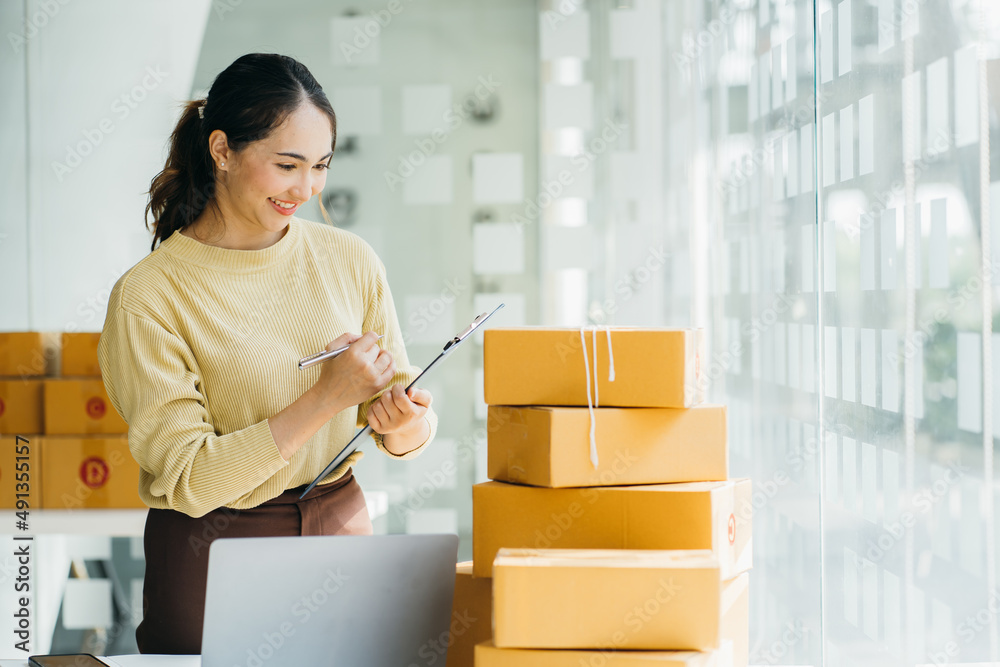 Young asia seller woman happy work on laptop busy cellphone call chat to customer at home office des