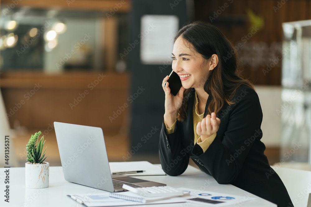 年轻的职场女性在办公室打电话。职场女性在电话里发短信，在lapt上工作