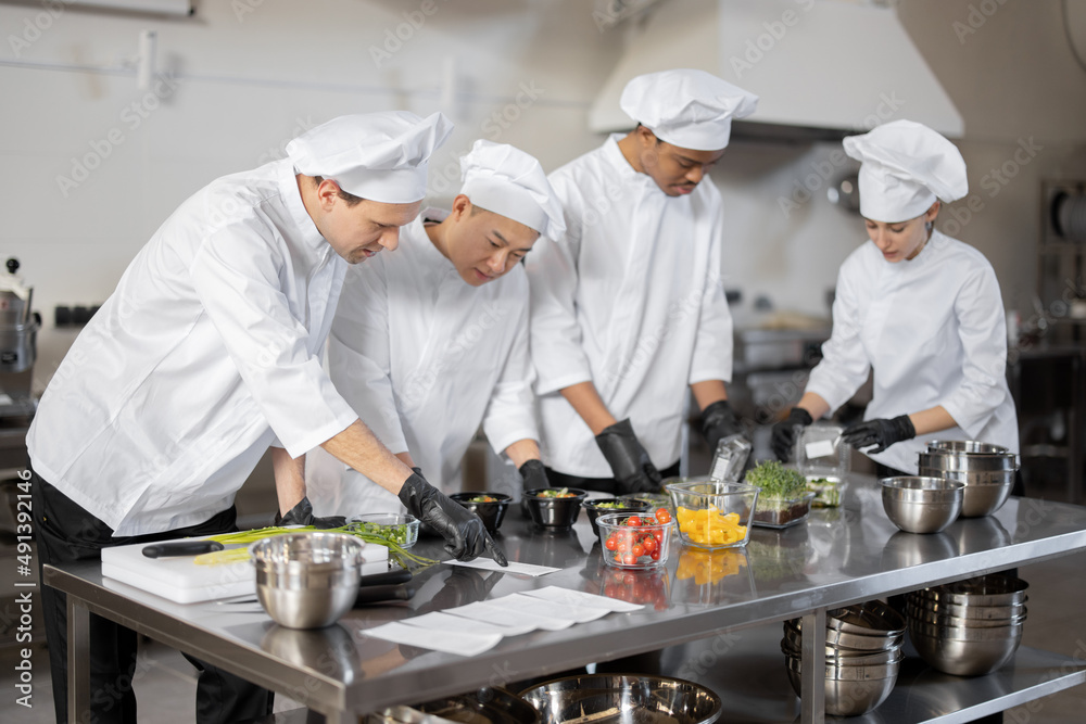 Multiracial team of cooks mixing ingredients for take away food in professional kitchen. Concept of 