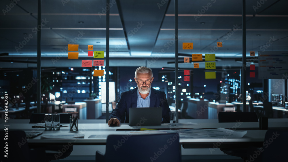 Successful Senior Businessman Working on Laptop Computer in Big City Office Late in the Evening. Inv