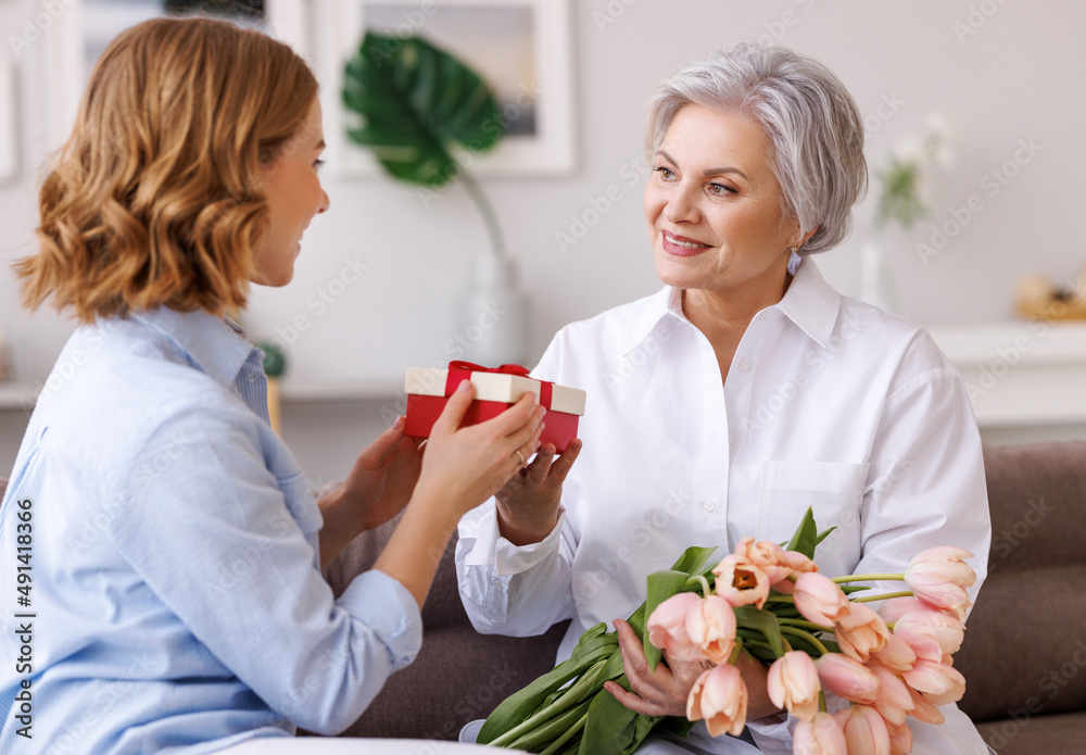 Delighted young woman congratulations mother with bouquet of fresh tulips