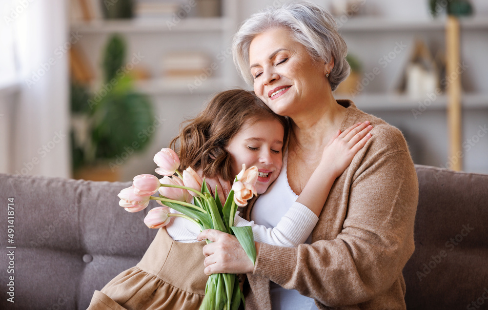 Gently little girl giving flowers  and gift to grandmother