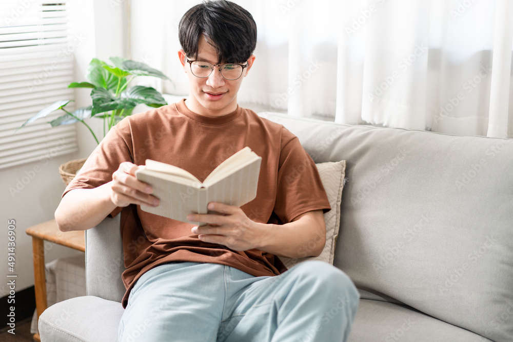 Technology Concept The male with his glasses sitting on the grey sofa, leaning his back on it, and r