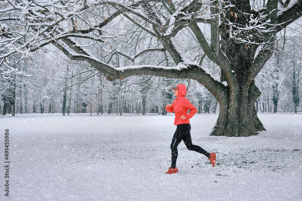 Running woman, girl runner on snow in park in winter sunny day.