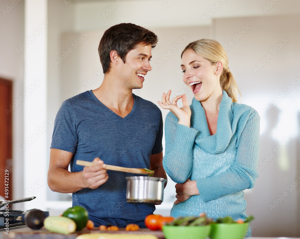 Perfecto. Shot of a handsome young man giving his wife a taste of his cooking.