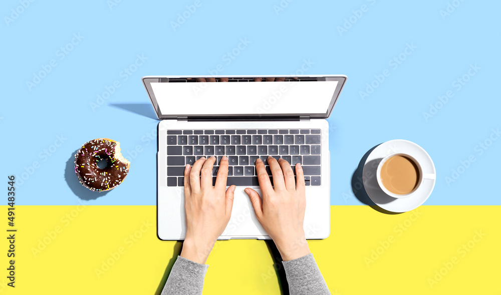 Person using a laptop computer with a donut and a cup of coffee - Flat lay