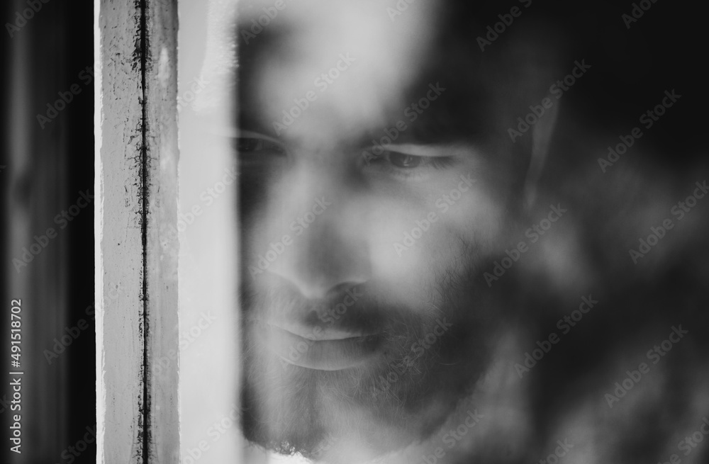 Blurred viewpoint. Closeup of a thoughtful young man seen through a window.