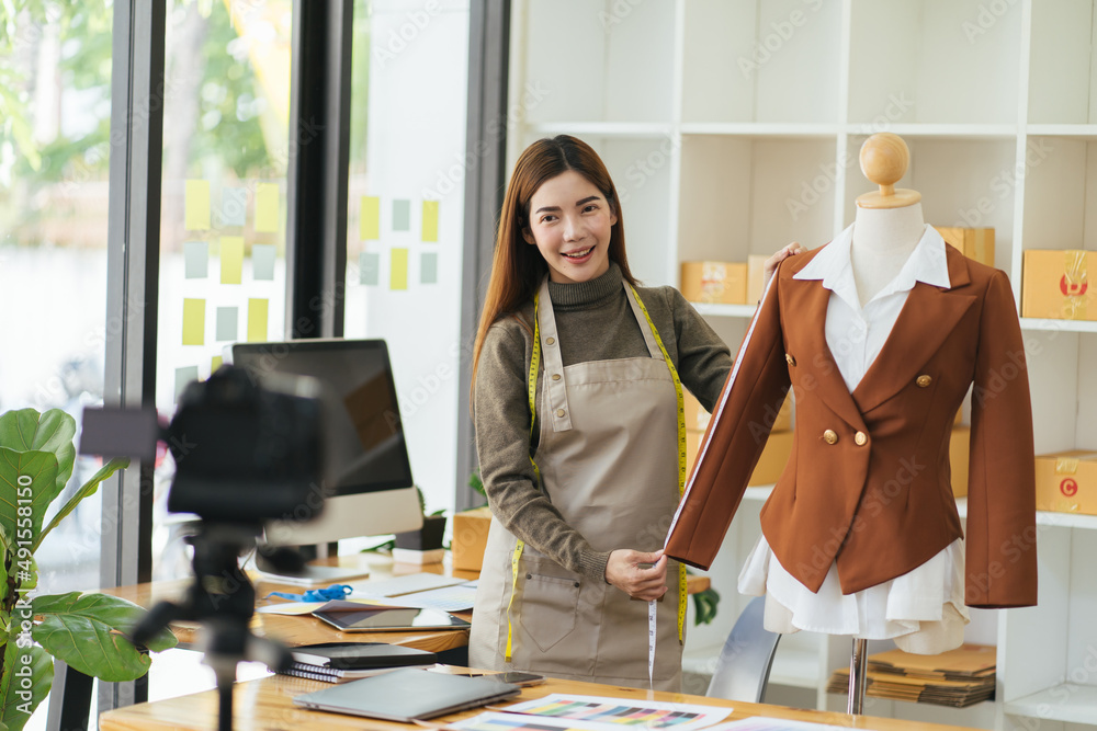 年轻的亚洲女士时装设计师使用手机接收订单并展示服装记录