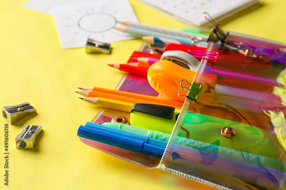 Stylish pencil case with different stationery on yellow background, closeup