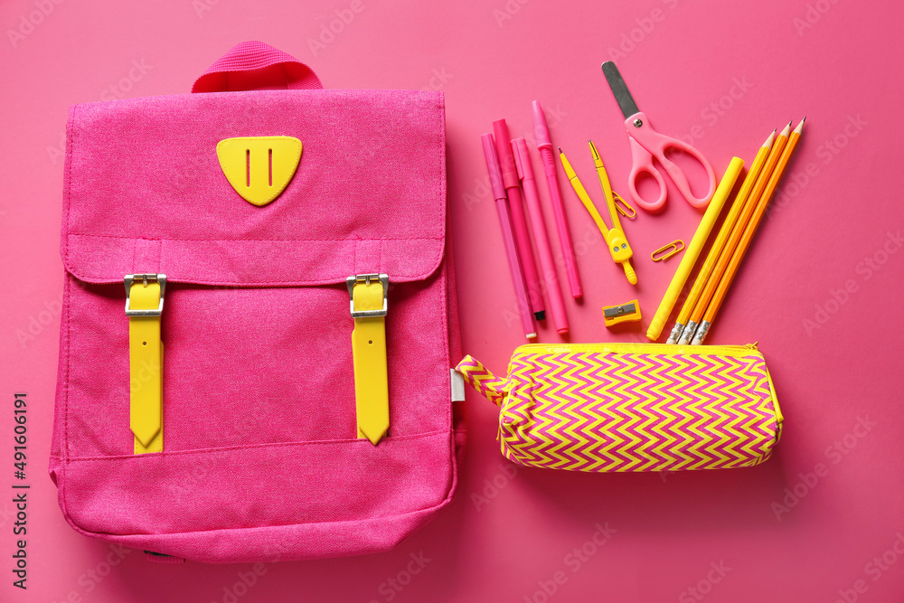 Pencil case with stationery and backpack on pink background