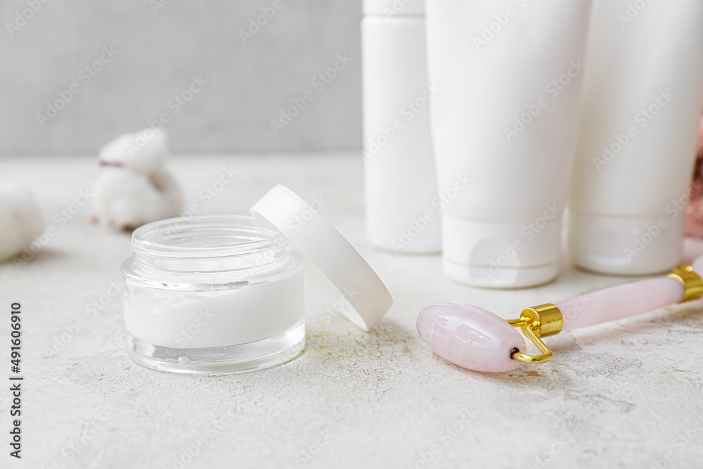 Jar of cosmetic product and facial massage tool on light background, closeup