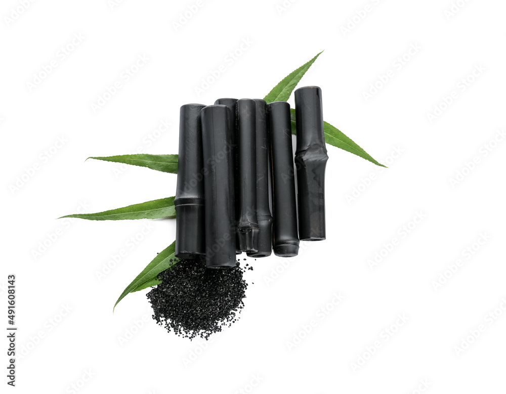 Composition with black bamboo sticks, activated carbon powder and leaves on white background