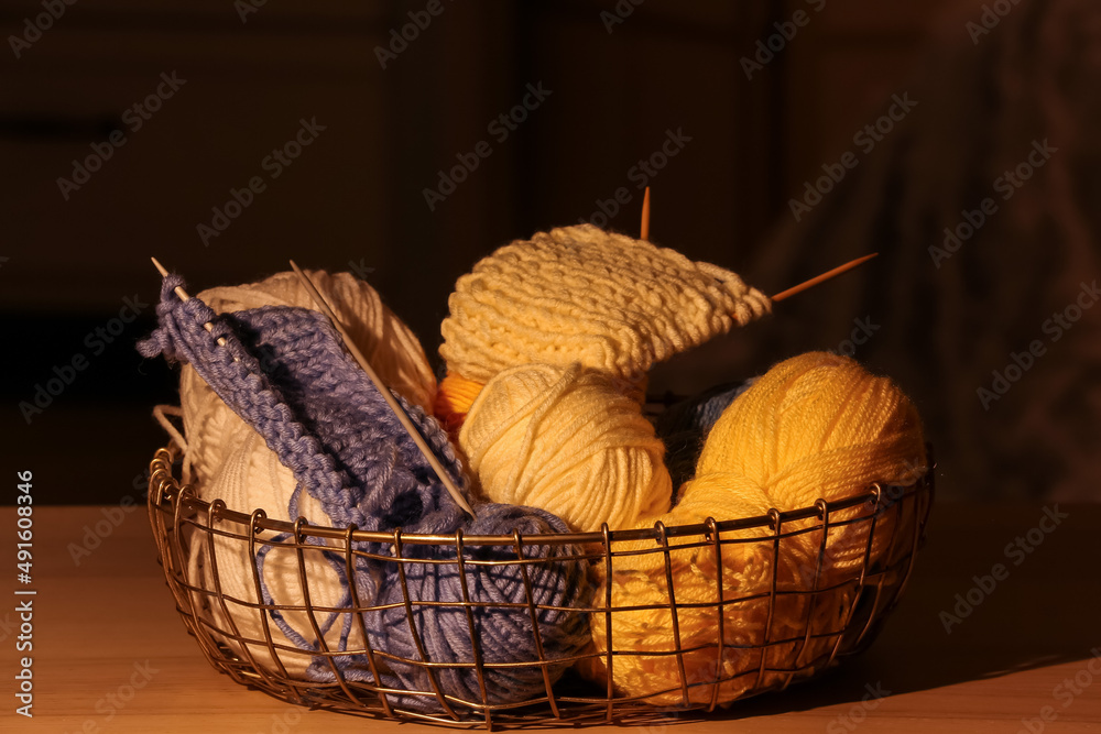 Basket with different yarn and needles on table