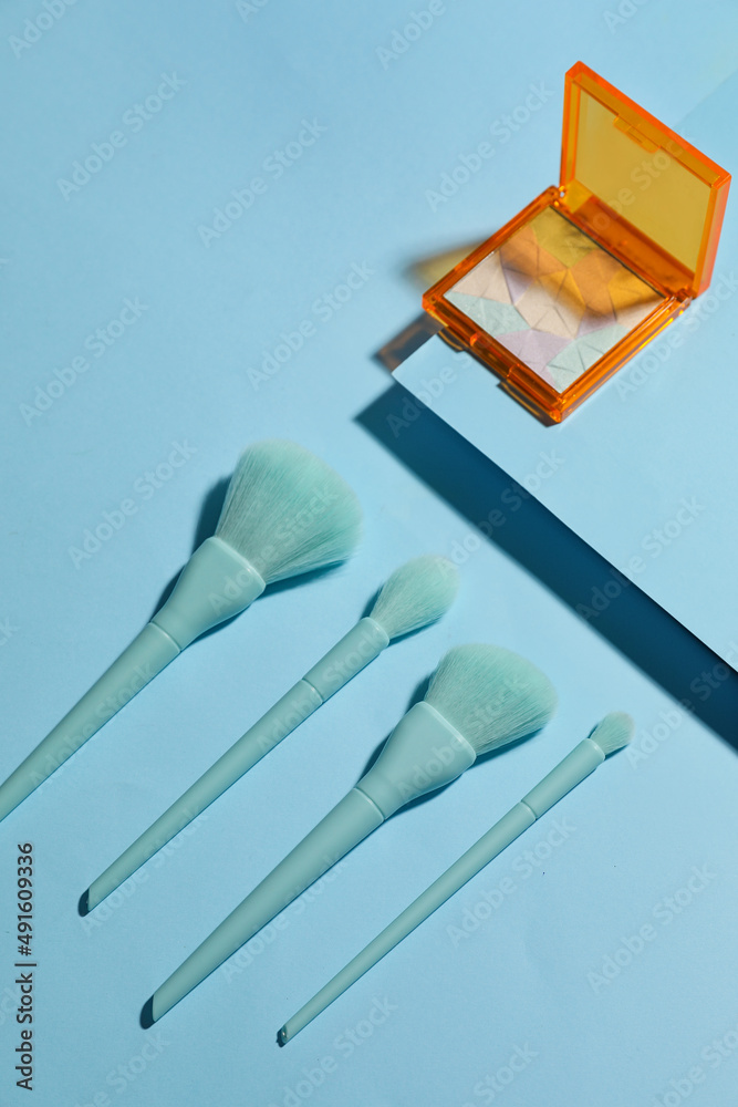 Set of makeup brushes and highlighter on blue background