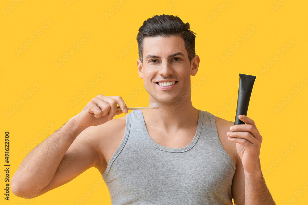 Handsome young man with activated charcoal tooth paste and brush on yellow background