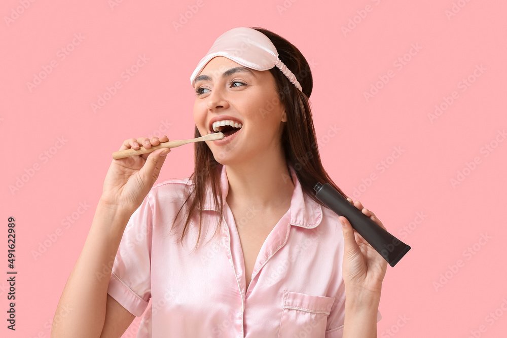 Beautiful young woman brushing teeth with activated charcoal tooth paste on pink background