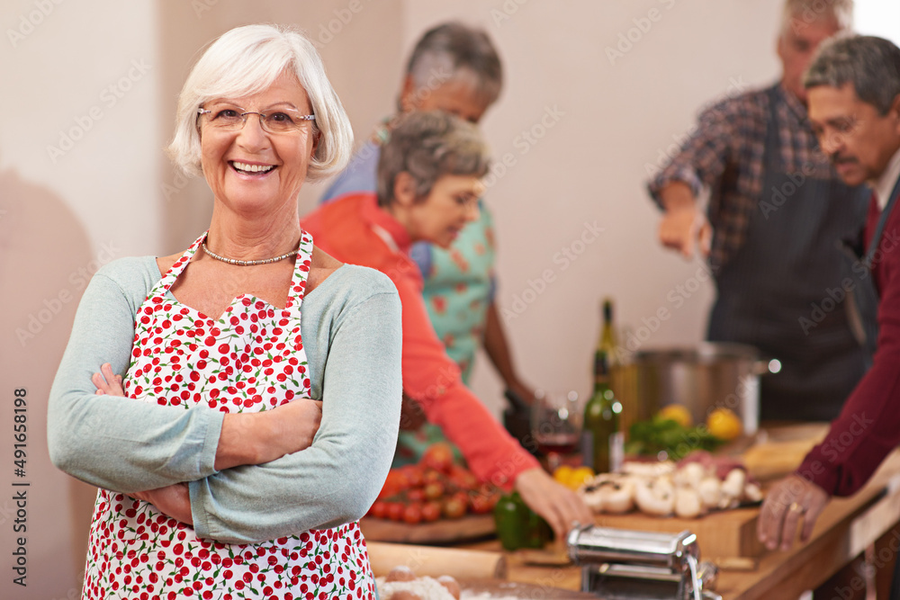 I love throwing dinner parties. Portrait of a senior woman with friends cooking together in the back