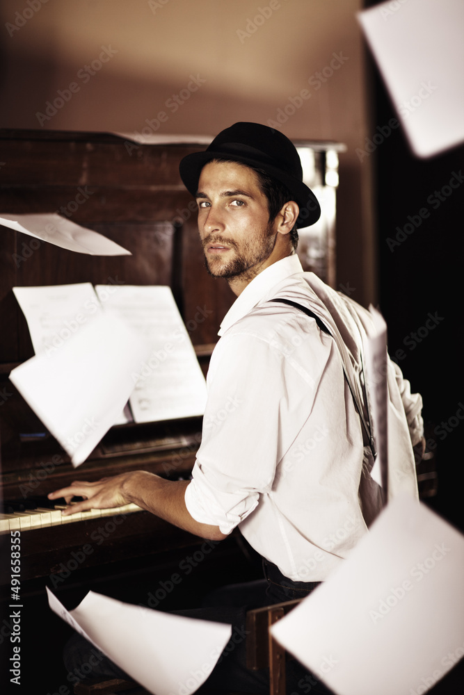 Musical inspiration. Portrait of a handsome young musician sitting at a piano with sheet music falli