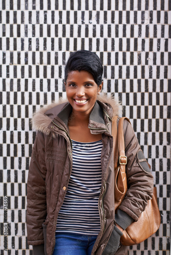 Winter street style. A portrait of a stylish young woman standing against a checkered wall.