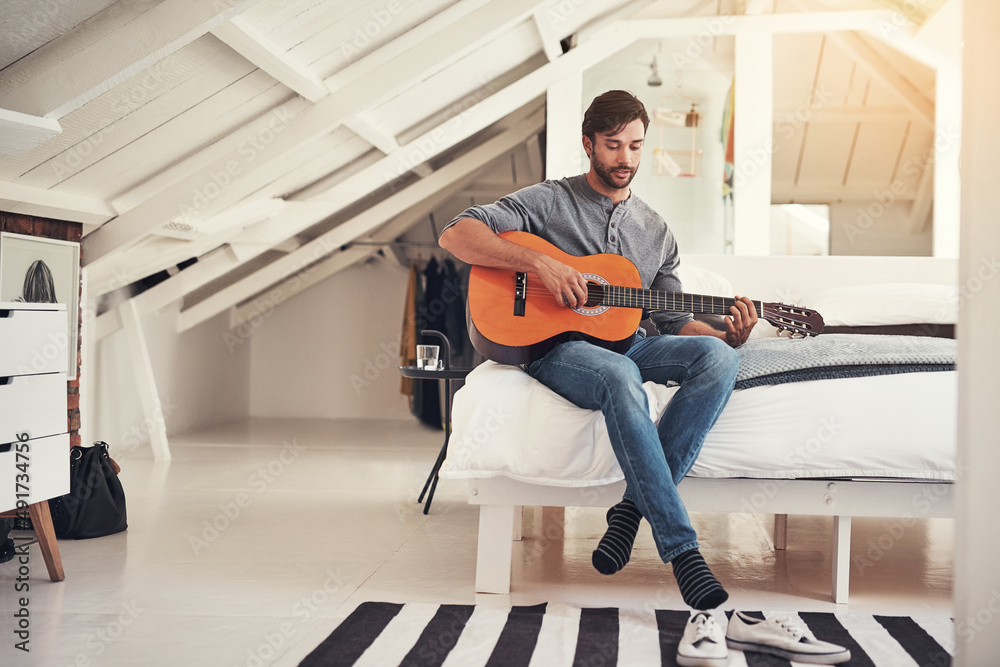 Music is his passion. Shot of a handsome young man practising guitar at home.