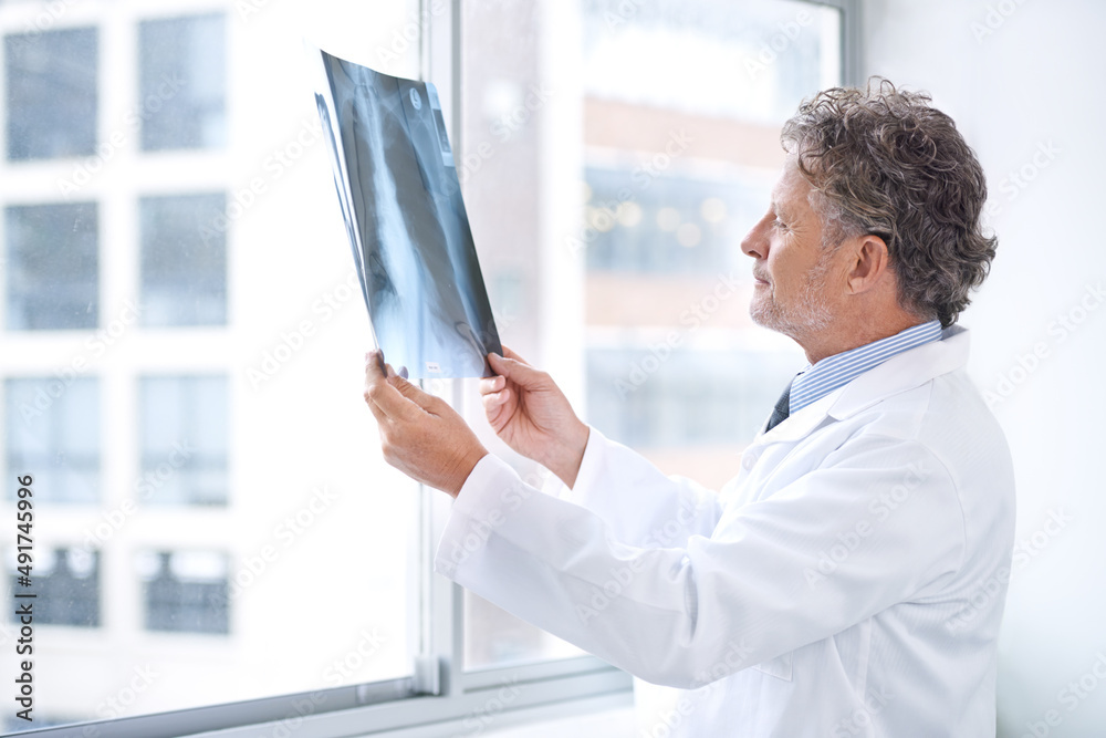 Hes got the inside information to your health. Shot of a mature doctor examining an x ray in his off