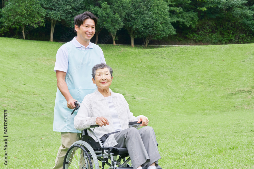 車椅子に乗った高齢者と介護士　屋外