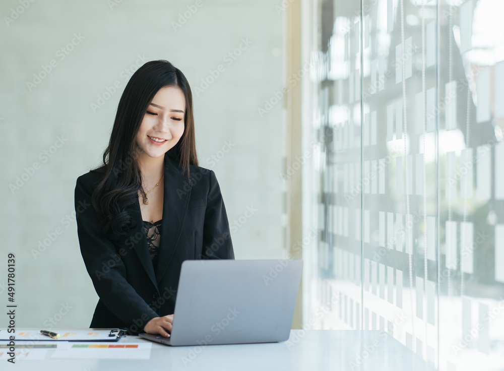 一位年轻的亚洲美女微笑着看着笔记本电脑屏幕的特写照片