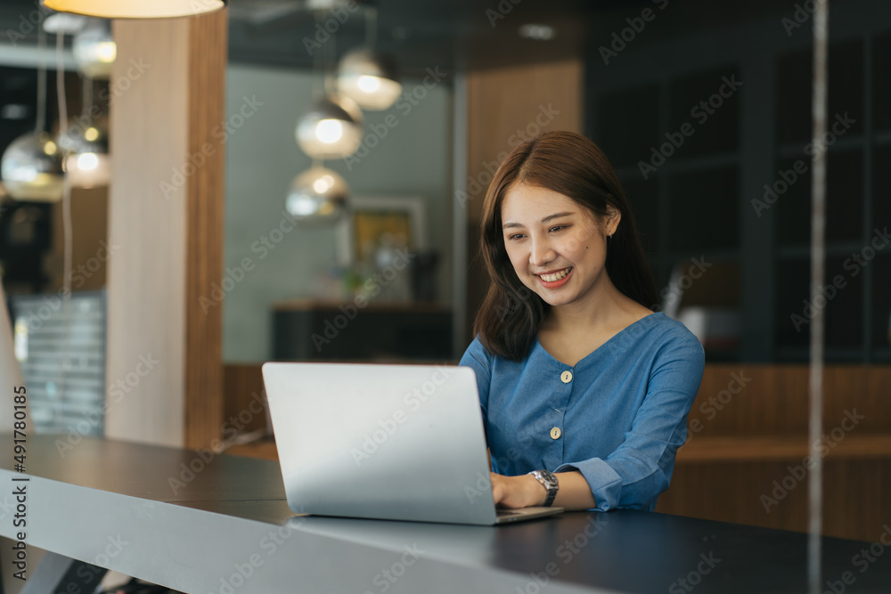 年轻的亚洲女学生坐在桌子旁做笔记和使用笔记本电脑。