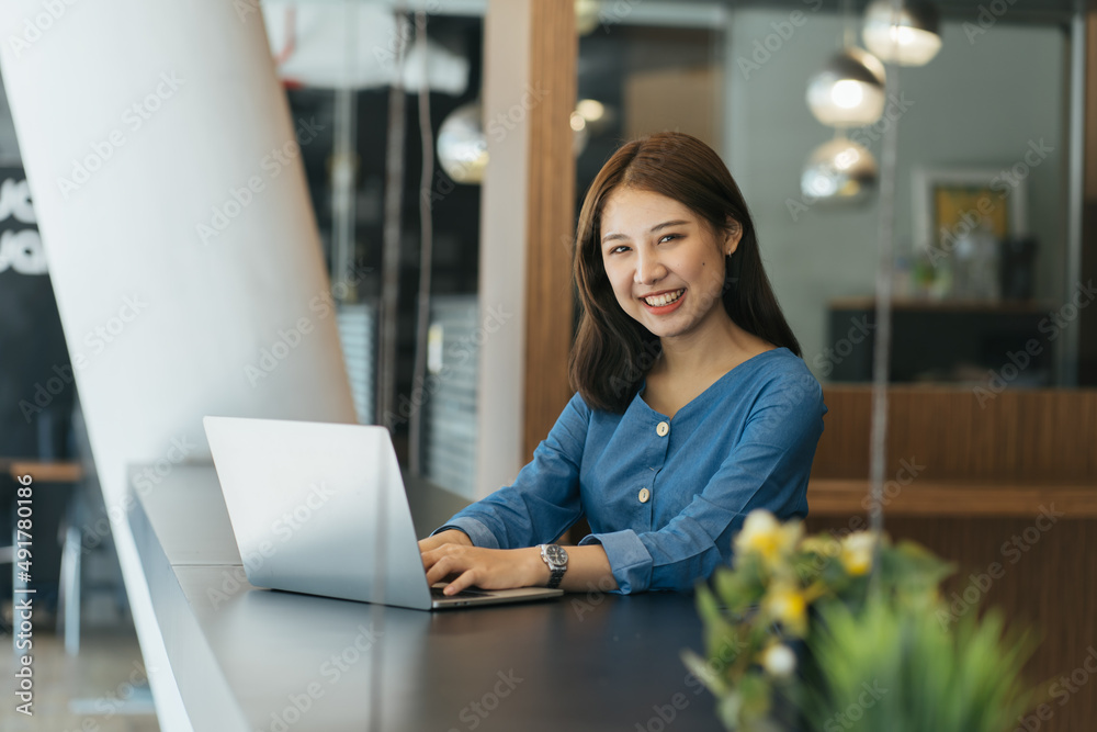 年轻的亚洲女学生坐在桌子旁做笔记和使用笔记本电脑。