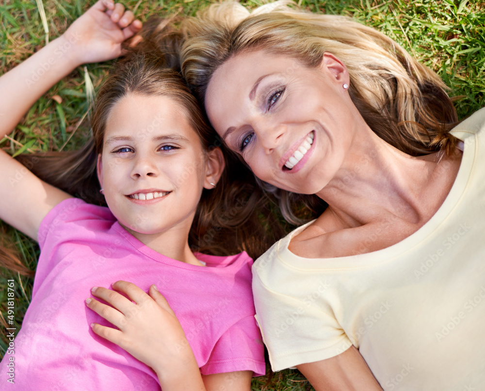 Spending time with mom. A happy mother and her young daughter lying on the grass together outdoors a