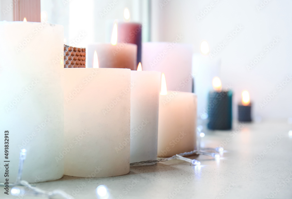 Many burning candles with glowing garland on windowsill, closeup