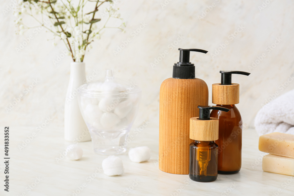 Bottles of cosmetic products, cotton balls and soap on light background