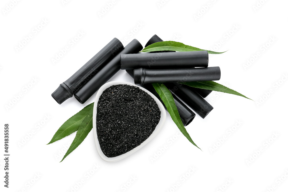 Bowl of activated carbon powder and bamboo sticks on white background