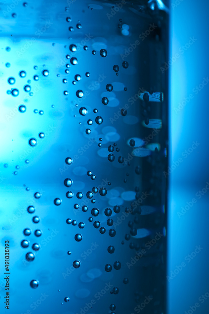 Glass of clear water with bubbles on blue background, closeup