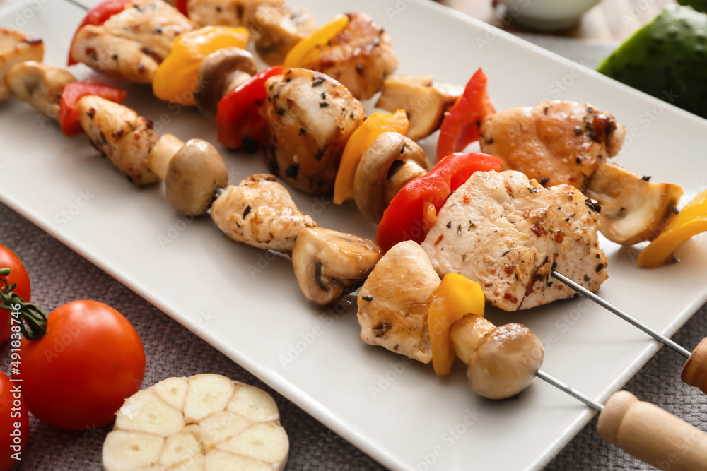 Plate of grilled chicken skewers with vegetables on table, closeup