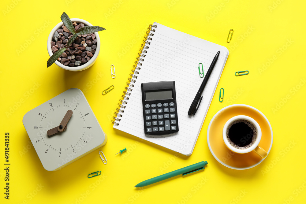 New alarm clock, cup of coffee, houseplant and stationery on yellow background