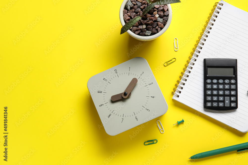 New alarm clock with houseplant and stationery on yellow background