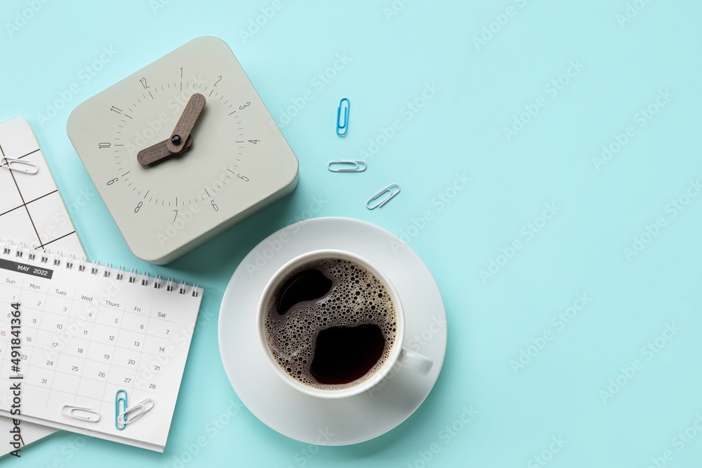 New alarm clock with cup of coffee and stationery on blue background