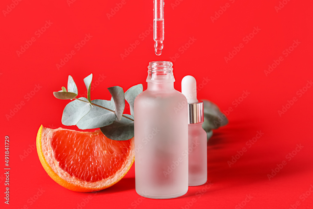 Dripping of grapefruit essential oil from pipette into bottle on color background, closeup