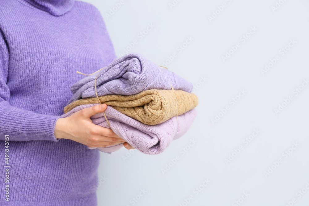 Woman with stack of knitted sweaters on light background