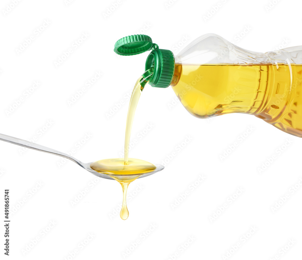 Pouring cooking oil from plastic bottle into spoon isolated on white background.