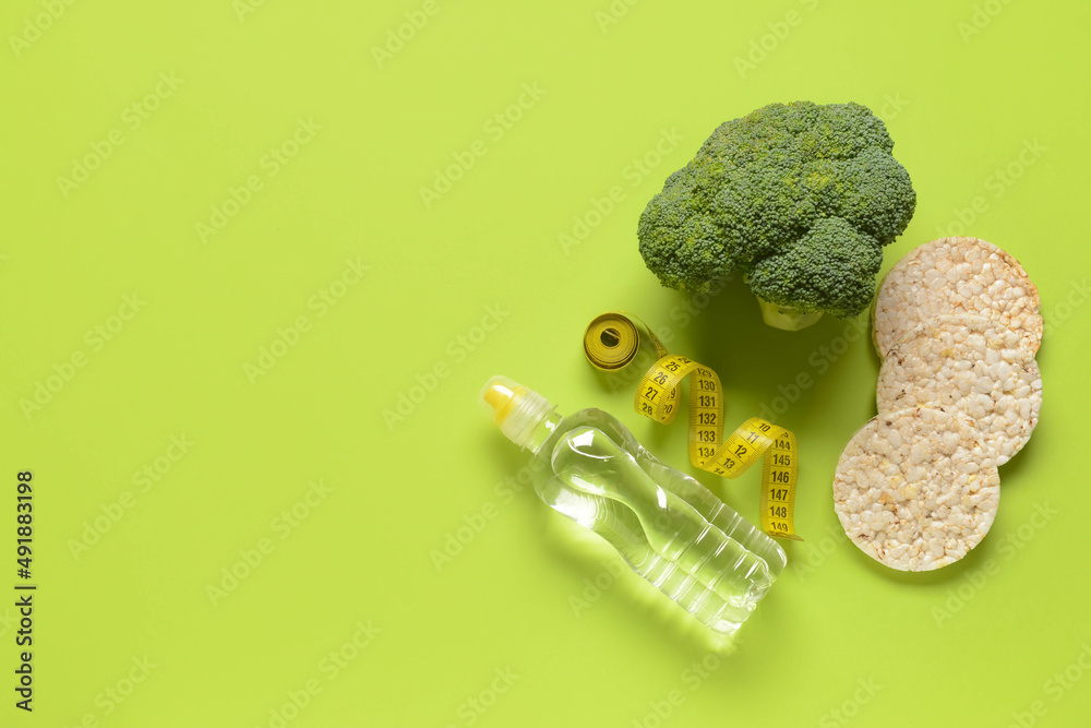 Bottle of water, crispbreads, measuring tape and broccoli on green background