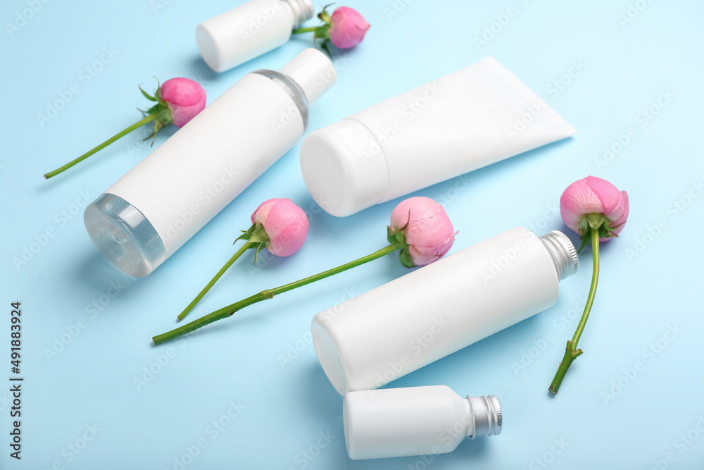 Different cosmetic products and beautiful rose flowers on blue background