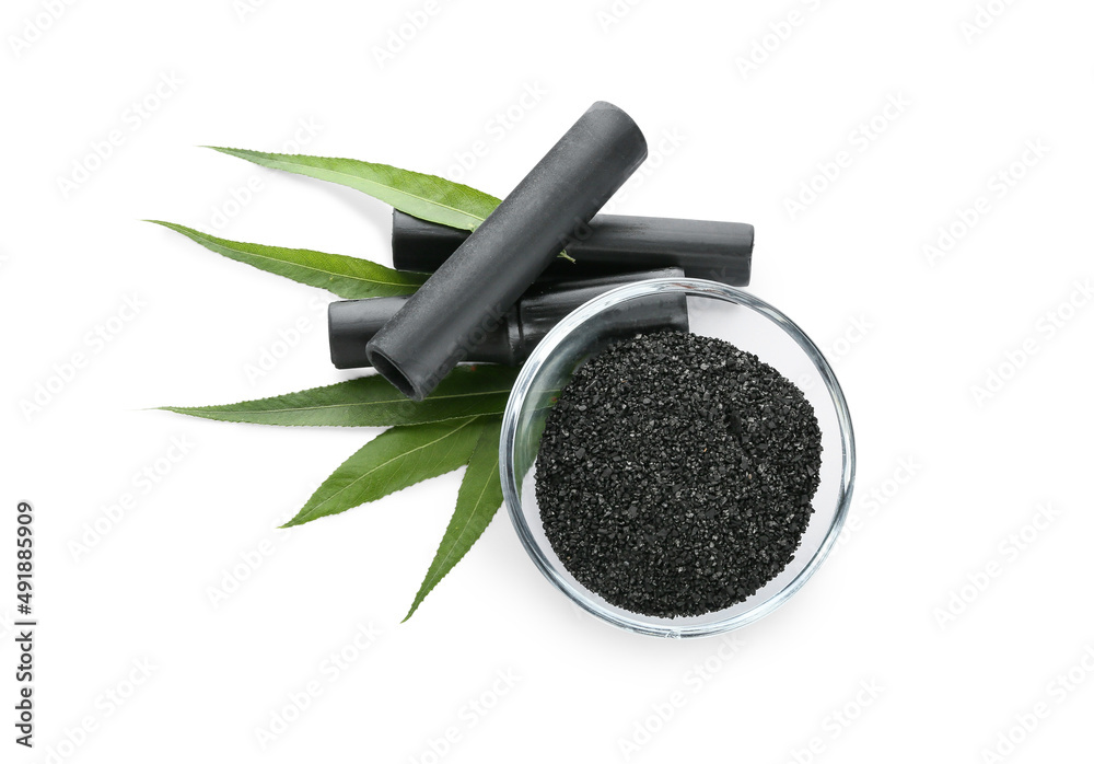 Glass bowl of activated carbon powder and black bamboo sticks on white background