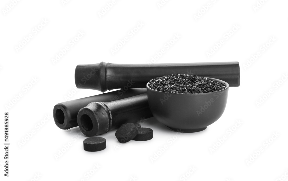 Bowl of activated carbon powder, pills and black bamboo sticks on white background