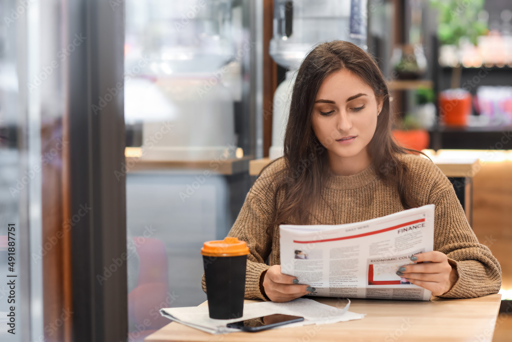 Pretty young woman reading newspaper at table in cafe