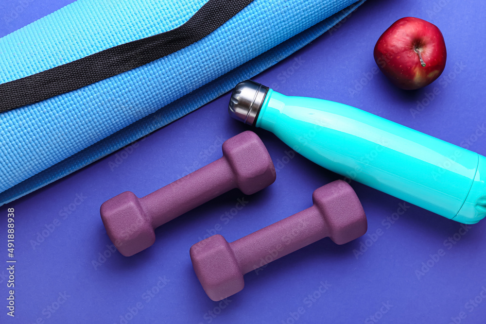 Stylish dumbbells, bottle, fitness mat and apple on blue background